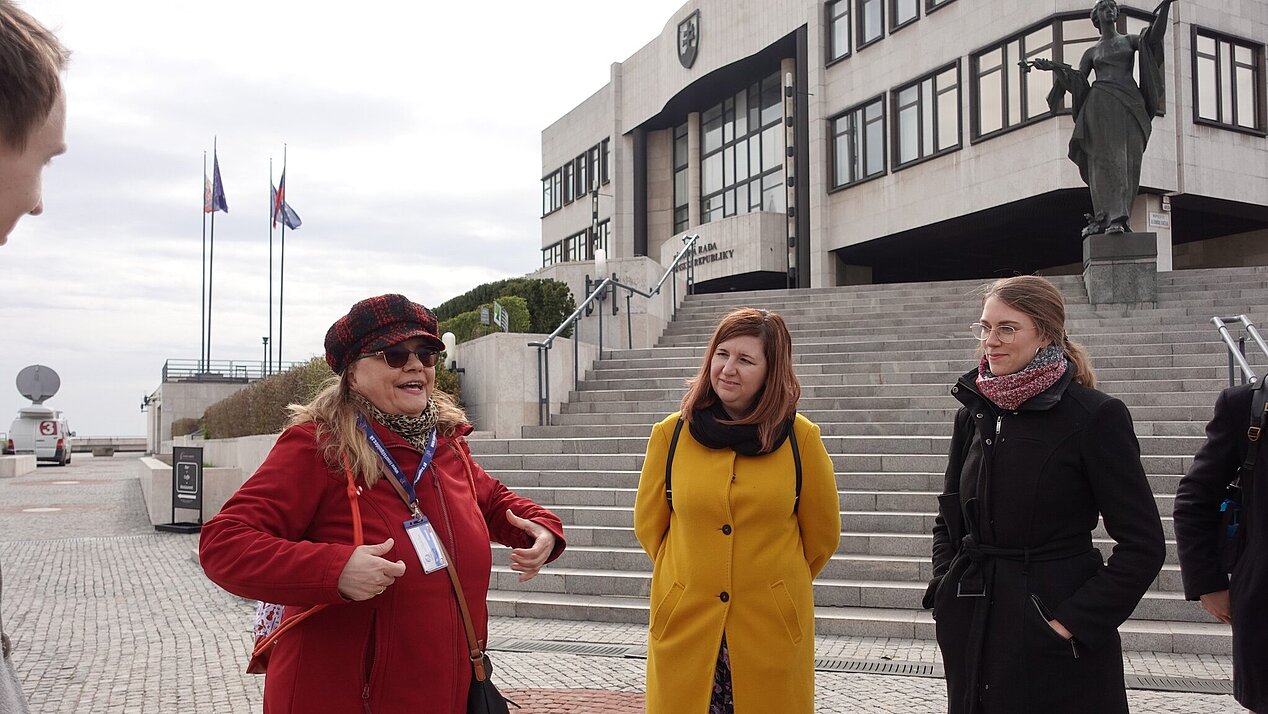 Drei Frauen sind zu sehen. Im Hintergrund ein Haus, eine Skulptur und eine Treppe. Impressionen vom Stadtrundgang in Bratislava während der Regionalwoche des ifa Bereichs Integration und Medien.